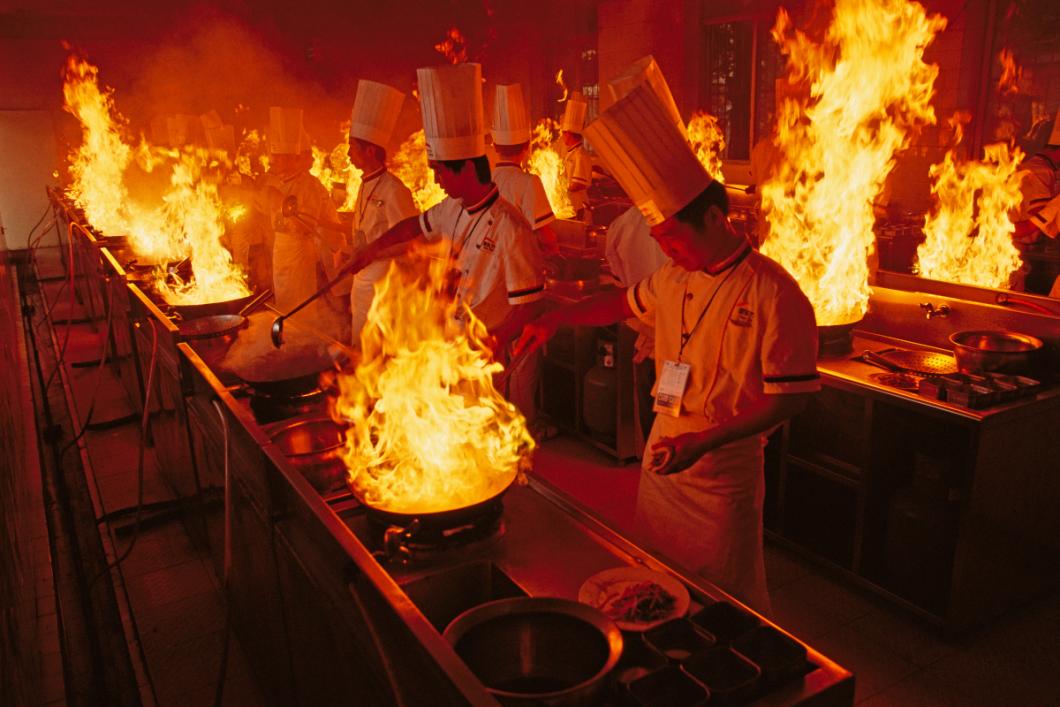 Rows of student chefs supervise the flames that blossom from their woks while they practice preparing vegetables at blistering temperatures. PHOTO BY FRITZ HOFFMAN; HEFEI, CHINA